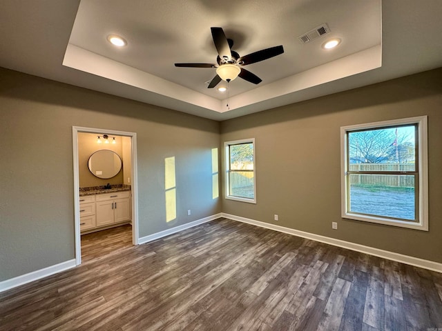 unfurnished bedroom featuring dark hardwood / wood-style flooring, a raised ceiling, and ensuite bath