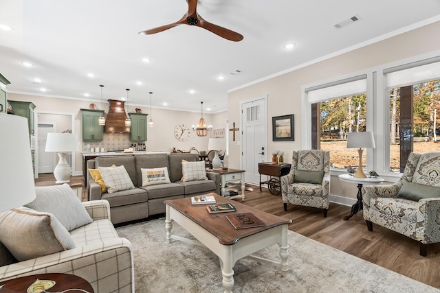 living room featuring hardwood / wood-style floors, ceiling fan with notable chandelier, and crown molding