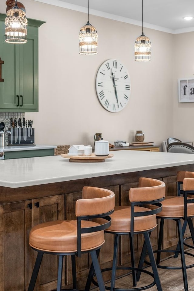 bar featuring pendant lighting, crown molding, hardwood / wood-style floors, and green cabinetry