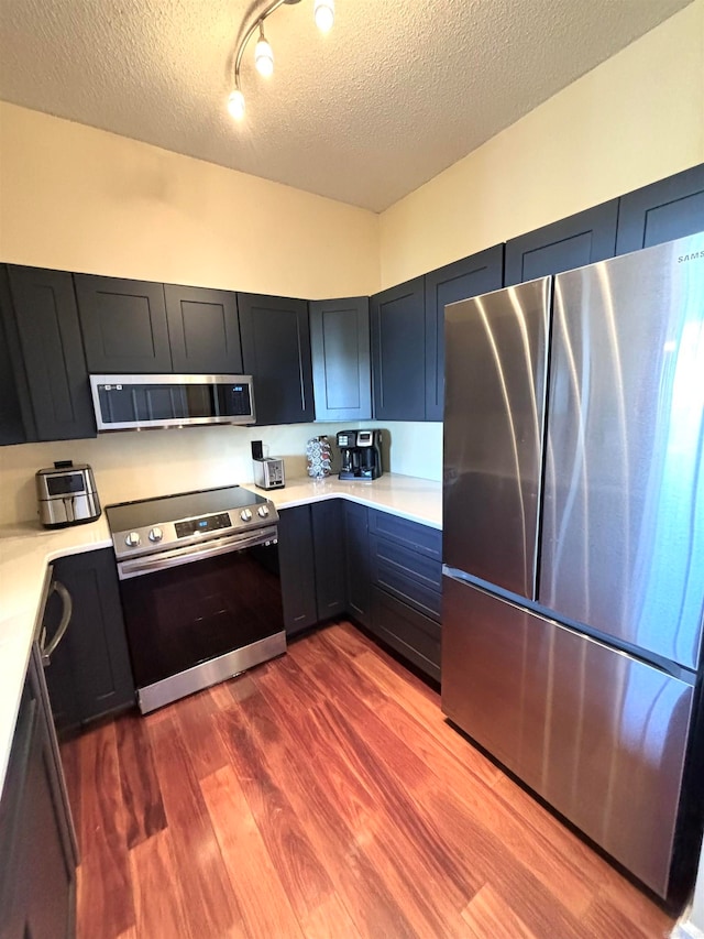 kitchen with rail lighting, stainless steel appliances, a textured ceiling, and wood-type flooring