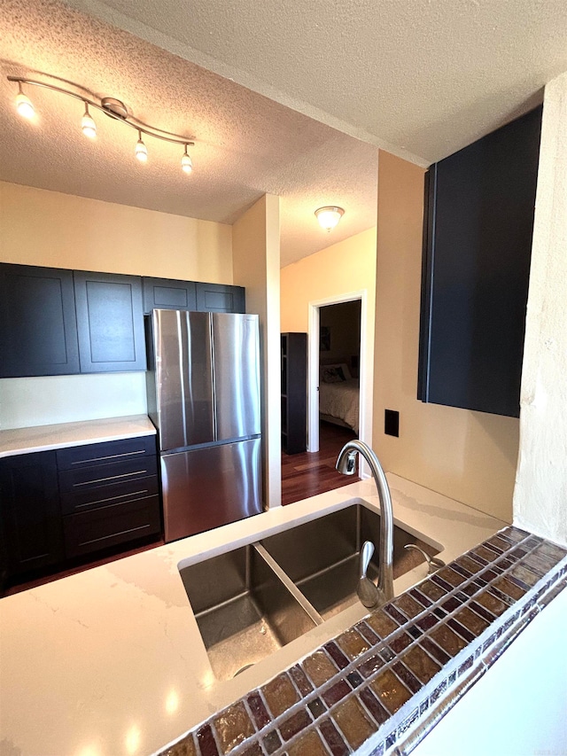 kitchen featuring stainless steel fridge, sink, and a textured ceiling