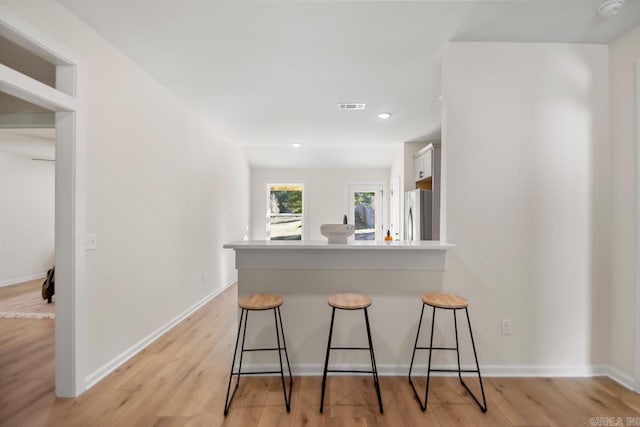 kitchen featuring white cabinetry, a kitchen breakfast bar, kitchen peninsula, stainless steel fridge, and light wood-type flooring