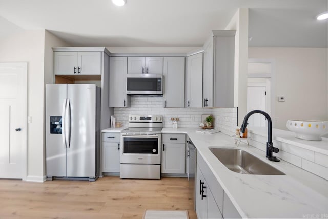 kitchen with tasteful backsplash, light stone counters, stainless steel appliances, sink, and light hardwood / wood-style floors