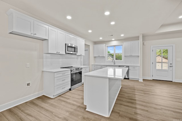 kitchen with white cabinets, appliances with stainless steel finishes, light hardwood / wood-style flooring, and a kitchen island