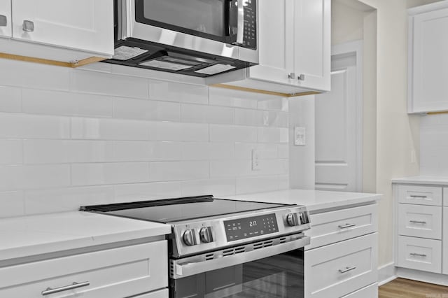 kitchen featuring light stone countertops, white cabinets, wood-type flooring, and appliances with stainless steel finishes