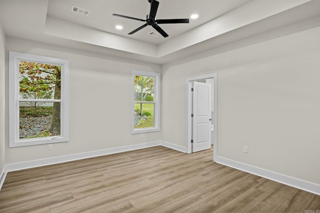 spare room featuring plenty of natural light, ceiling fan, light wood-type flooring, and a tray ceiling