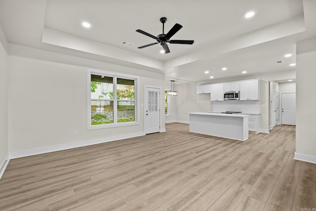 unfurnished living room featuring ceiling fan with notable chandelier, light hardwood / wood-style floors, and a tray ceiling