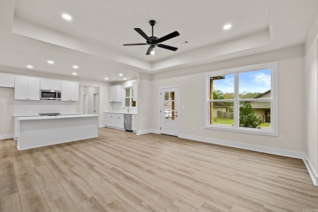 unfurnished living room with ceiling fan, a raised ceiling, sink, and light hardwood / wood-style flooring