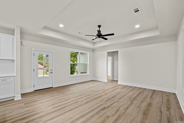 unfurnished living room featuring ceiling fan, a tray ceiling, and light hardwood / wood-style flooring