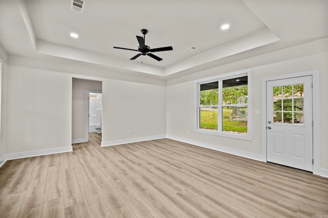 unfurnished living room with light hardwood / wood-style floors, a raised ceiling, and ceiling fan