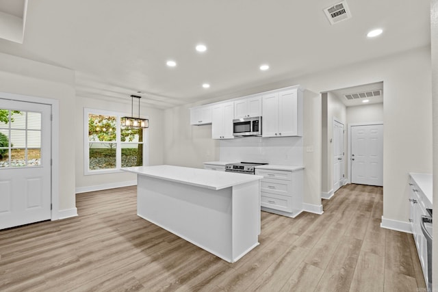 kitchen featuring appliances with stainless steel finishes, light wood-type flooring, a center island, white cabinetry, and hanging light fixtures