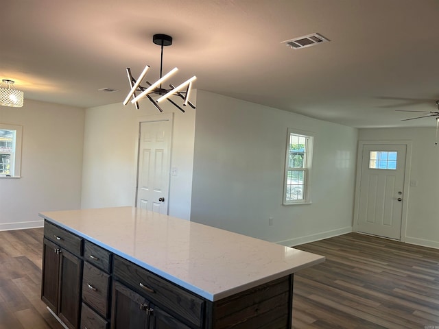 kitchen with light stone countertops, ceiling fan with notable chandelier, a center island, dark hardwood / wood-style floors, and hanging light fixtures