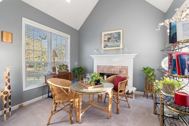 dining room with high vaulted ceiling, light colored carpet, a brick fireplace, and plenty of natural light