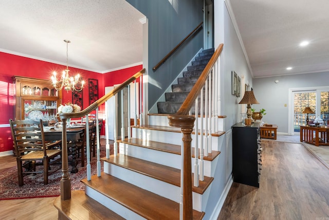 stairs with ornamental molding, a textured ceiling, hardwood / wood-style flooring, and a notable chandelier