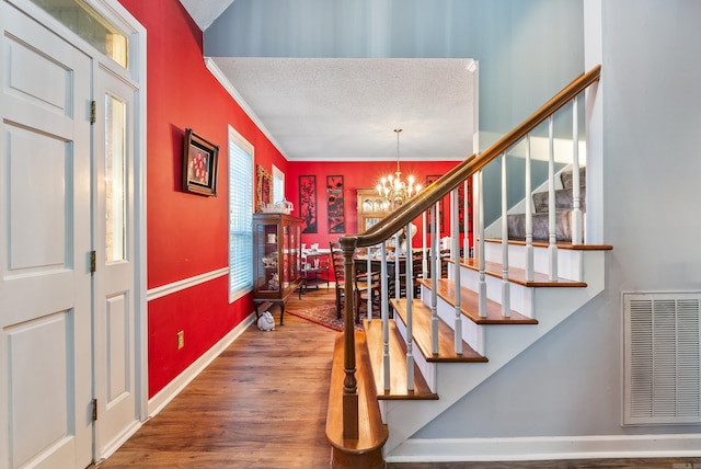 stairway featuring hardwood / wood-style floors, crown molding, a textured ceiling, and a chandelier