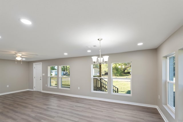 spare room with ceiling fan with notable chandelier and light hardwood / wood-style floors