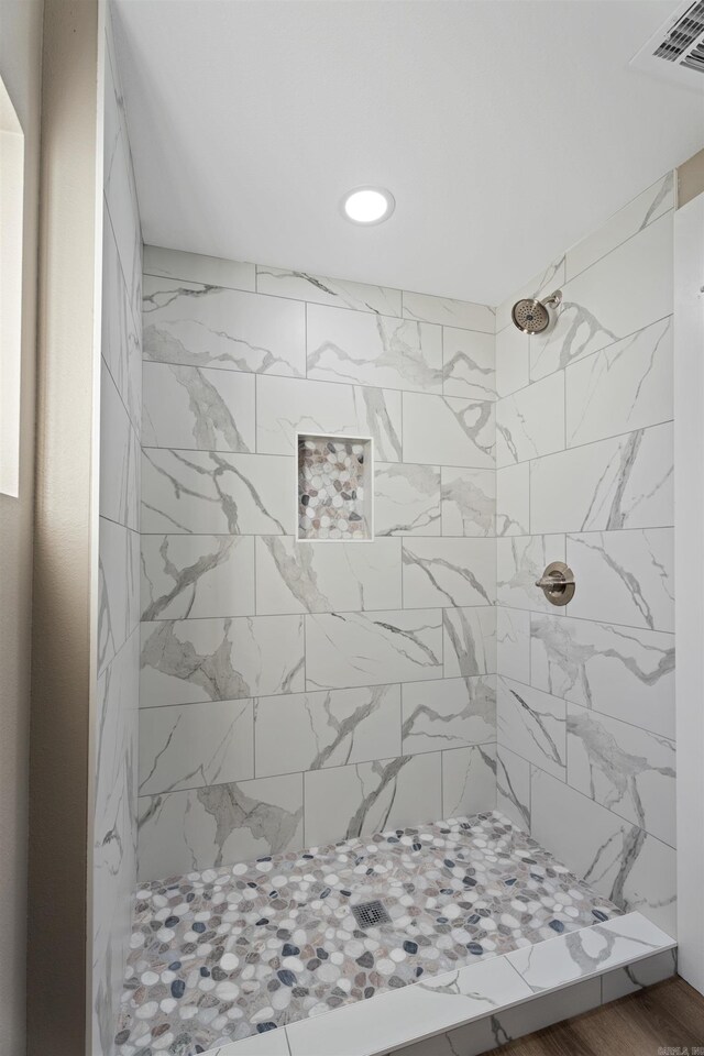 bathroom featuring a tile shower and wood-type flooring