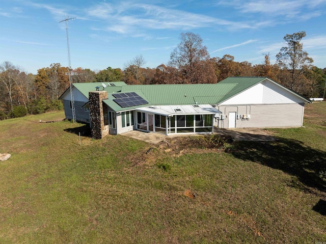 back of house featuring a lawn, a sunroom, and solar panels