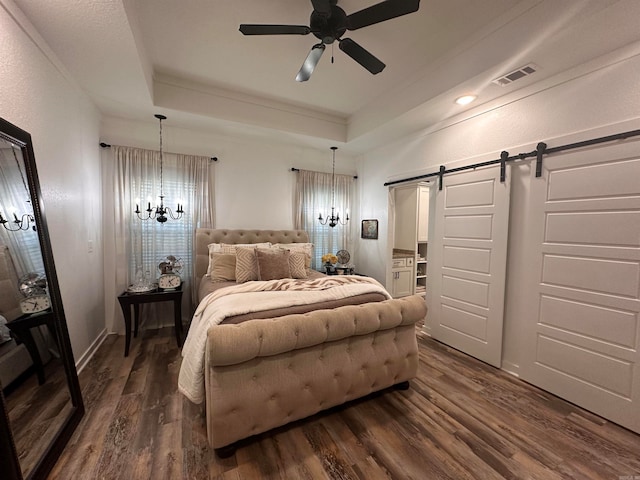 bedroom featuring ceiling fan with notable chandelier, a barn door, dark hardwood / wood-style flooring, and a tray ceiling