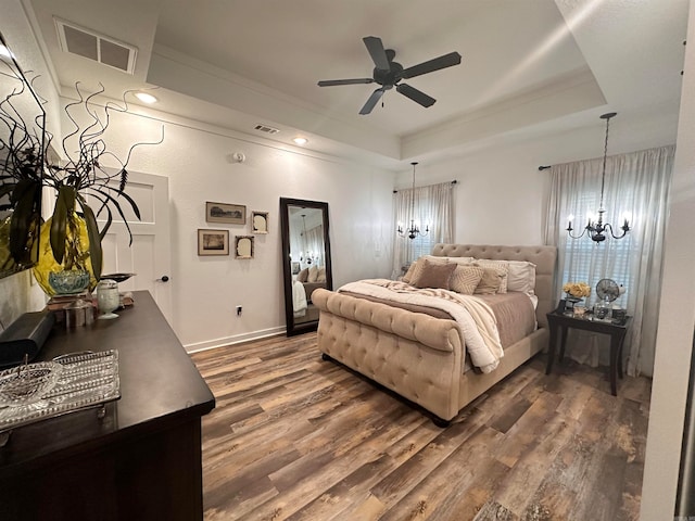 bedroom featuring ceiling fan with notable chandelier, a tray ceiling, and dark wood-type flooring