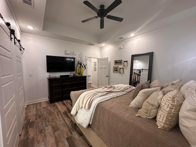 bedroom featuring dark hardwood / wood-style floors, ceiling fan, a raised ceiling, and a barn door