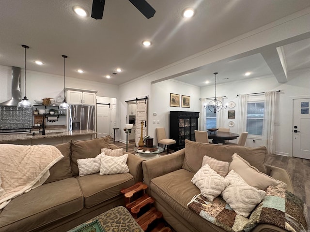 living room featuring ceiling fan with notable chandelier, sink, a barn door, ornamental molding, and wood-type flooring