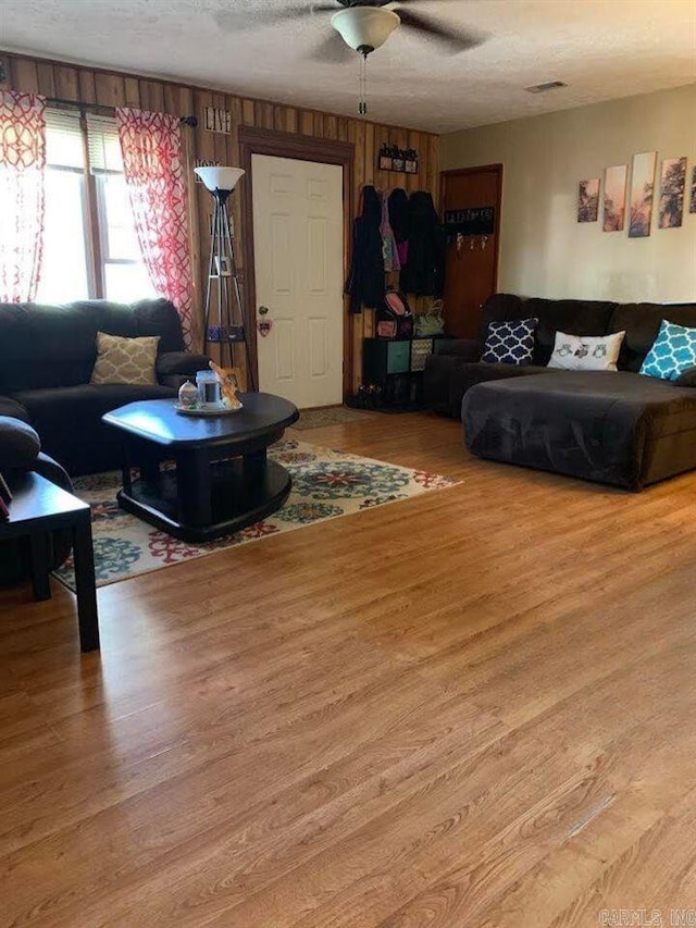 living room featuring hardwood / wood-style flooring, ceiling fan, wood walls, and a textured ceiling