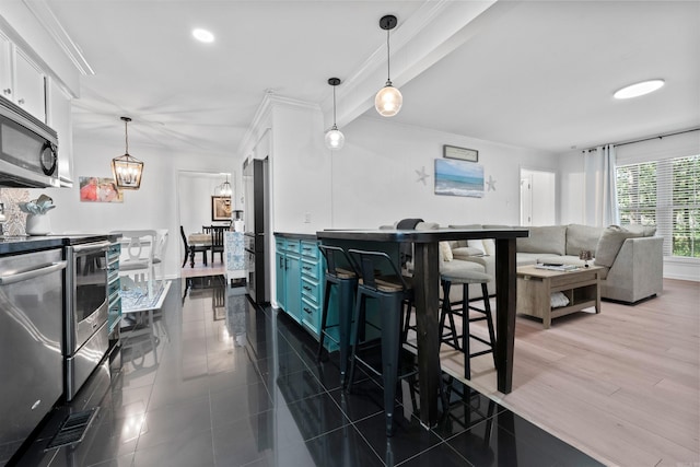 kitchen with a breakfast bar, white cabinetry, hanging light fixtures, and stainless steel appliances