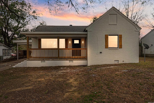 back house at dusk featuring a porch