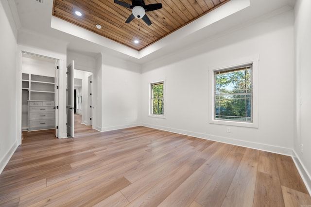 unfurnished bedroom with a tray ceiling, ceiling fan, light hardwood / wood-style flooring, and a spacious closet