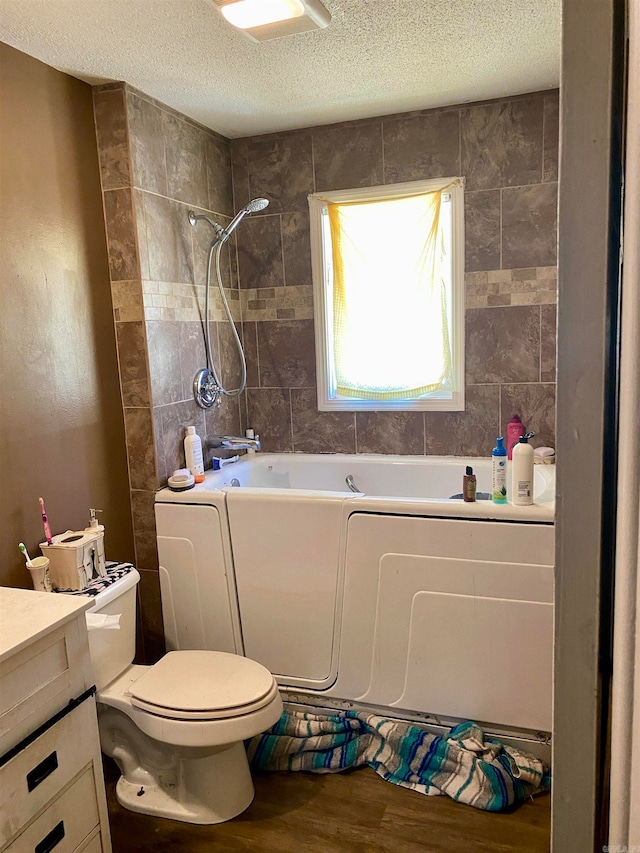 full bathroom featuring hardwood / wood-style floors, vanity, tiled shower / bath combo, toilet, and a textured ceiling