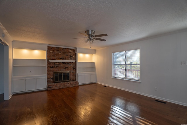 unfurnished living room with ceiling fan, dark wood-type flooring, a brick fireplace, crown molding, and a textured ceiling