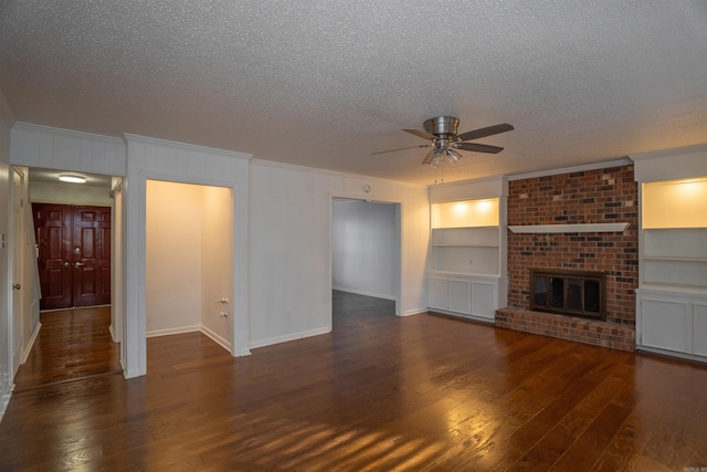 unfurnished living room with a brick fireplace, built in shelves, a textured ceiling, ceiling fan, and dark wood-type flooring