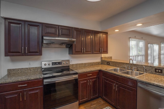 kitchen with sink, dark wood-type flooring, kitchen peninsula, stone countertops, and appliances with stainless steel finishes