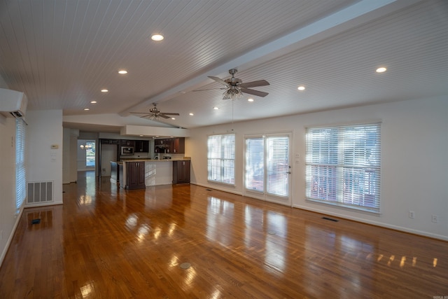 unfurnished living room with hardwood / wood-style floors, lofted ceiling with beams, an AC wall unit, and a healthy amount of sunlight