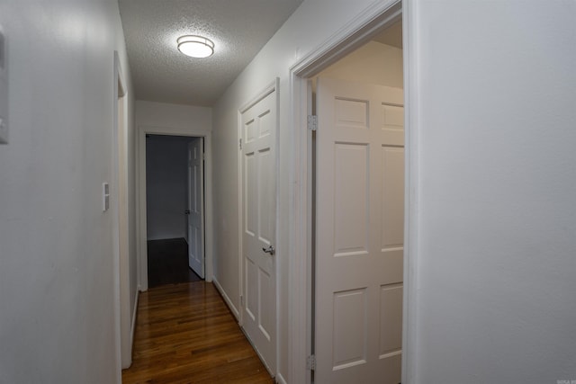 hallway with a textured ceiling and dark hardwood / wood-style floors