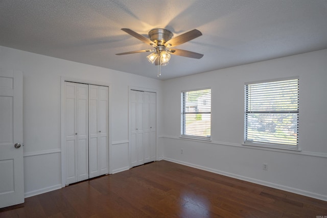 unfurnished bedroom featuring a textured ceiling, two closets, ceiling fan, and dark wood-type flooring