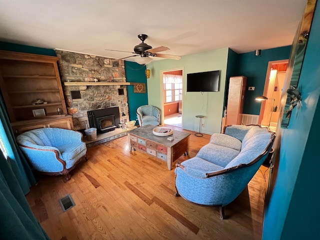 living room featuring light wood-type flooring, a wood stove, and ceiling fan