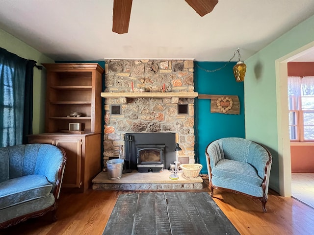 sitting room featuring a wood stove, ceiling fan, and hardwood / wood-style floors