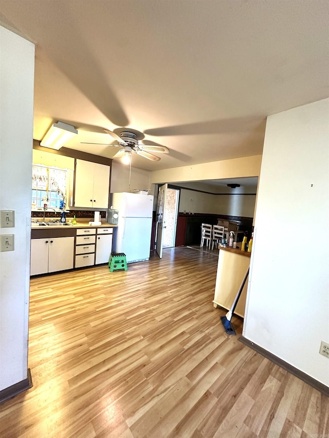 kitchen featuring ceiling fan, sink, white fridge, white cabinets, and light wood-type flooring