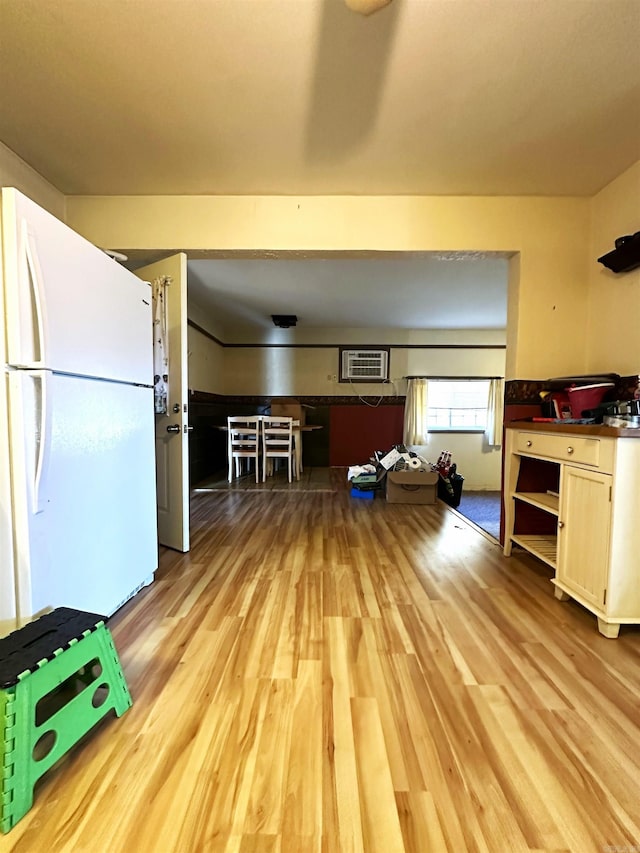 kitchen with white fridge, light wood-type flooring, white cabinetry, and an AC wall unit