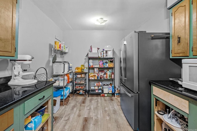 kitchen with dark stone counters, stainless steel fridge, and light hardwood / wood-style floors