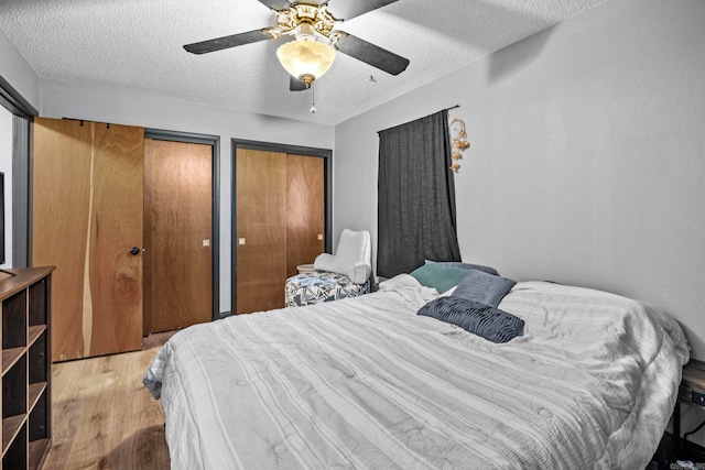 bedroom featuring multiple closets, ceiling fan, a textured ceiling, and light wood-type flooring