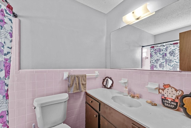 bathroom with a shower with curtain, a textured ceiling, toilet, vanity, and tile walls