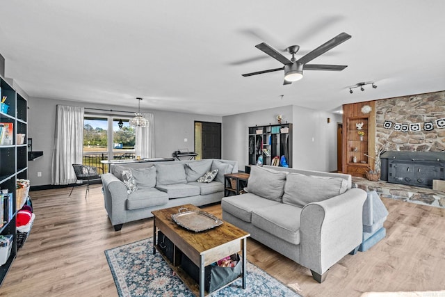 living room featuring ceiling fan with notable chandelier, light hardwood / wood-style floors, a wood stove, and track lighting