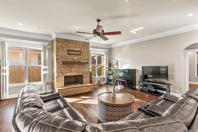 living room featuring ceiling fan, a stone fireplace, ornamental molding, and dark wood-type flooring