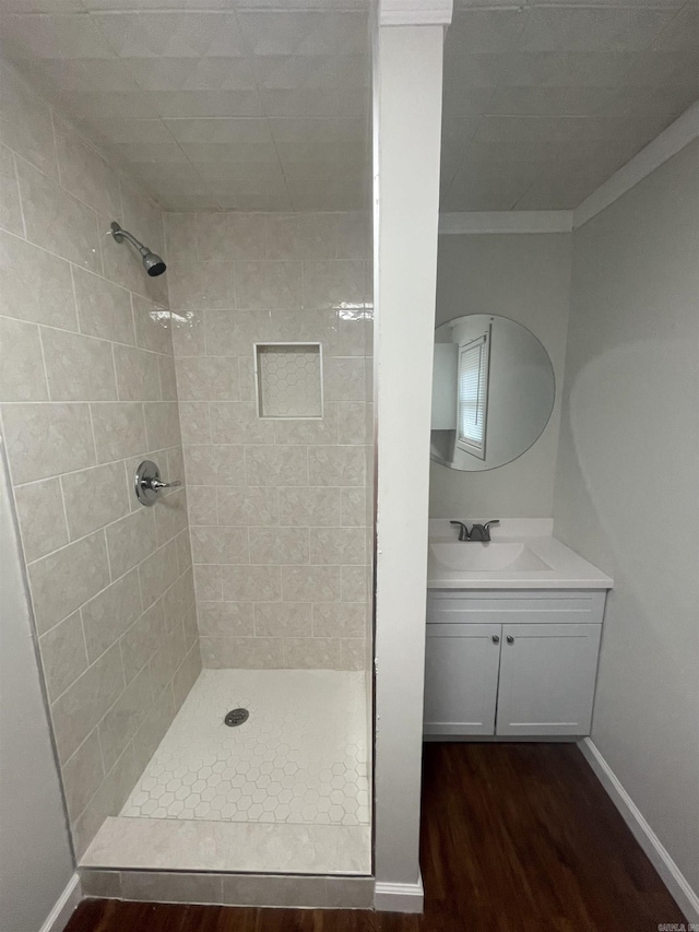 bathroom featuring hardwood / wood-style flooring, vanity, a tile shower, and crown molding