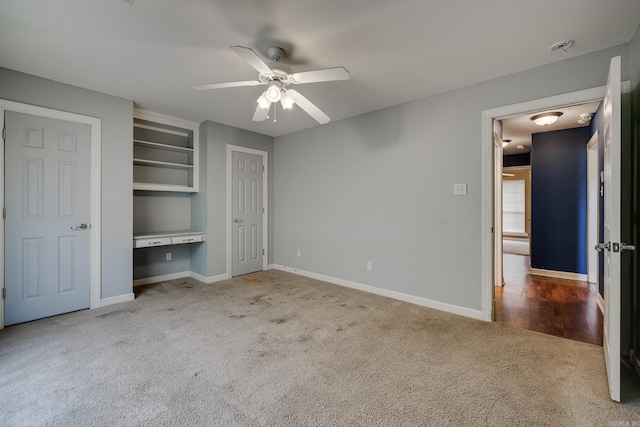 unfurnished bedroom featuring light carpet, built in desk, and ceiling fan