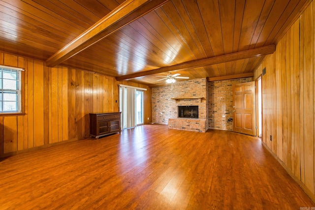 unfurnished living room with wood walls, wooden ceiling, ceiling fan, beam ceiling, and wood-type flooring