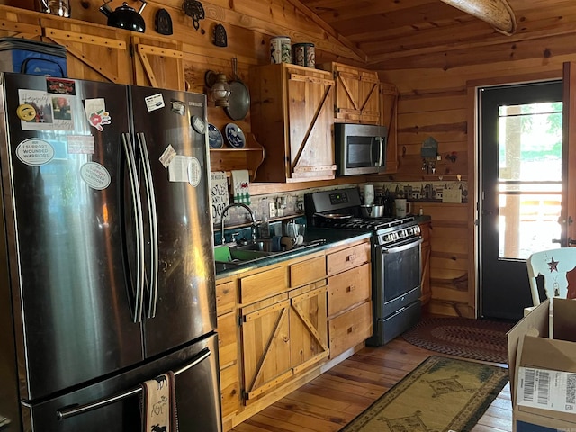 kitchen featuring appliances with stainless steel finishes, vaulted ceiling, wooden walls, sink, and light hardwood / wood-style floors